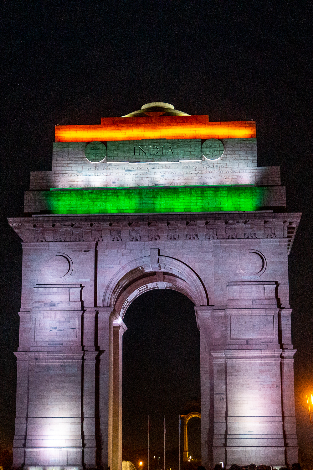 A night photo of India gate arch lit up with the orange, white, and green flag of India