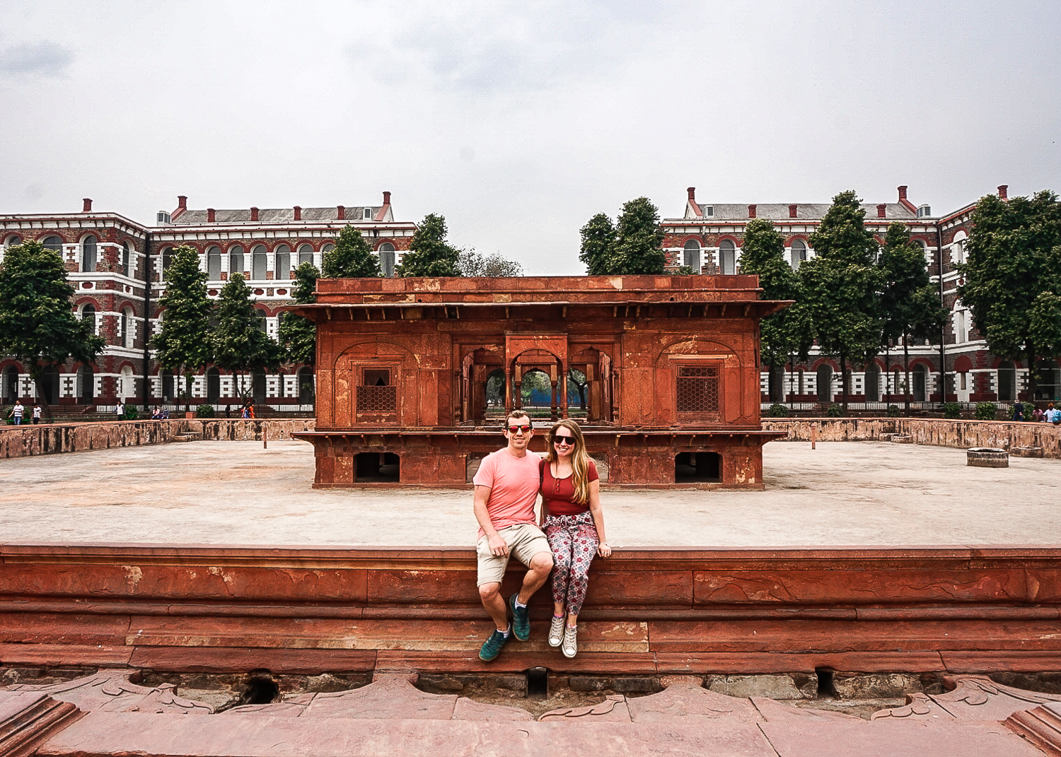 A couple sat on a wall by a red sandstone building