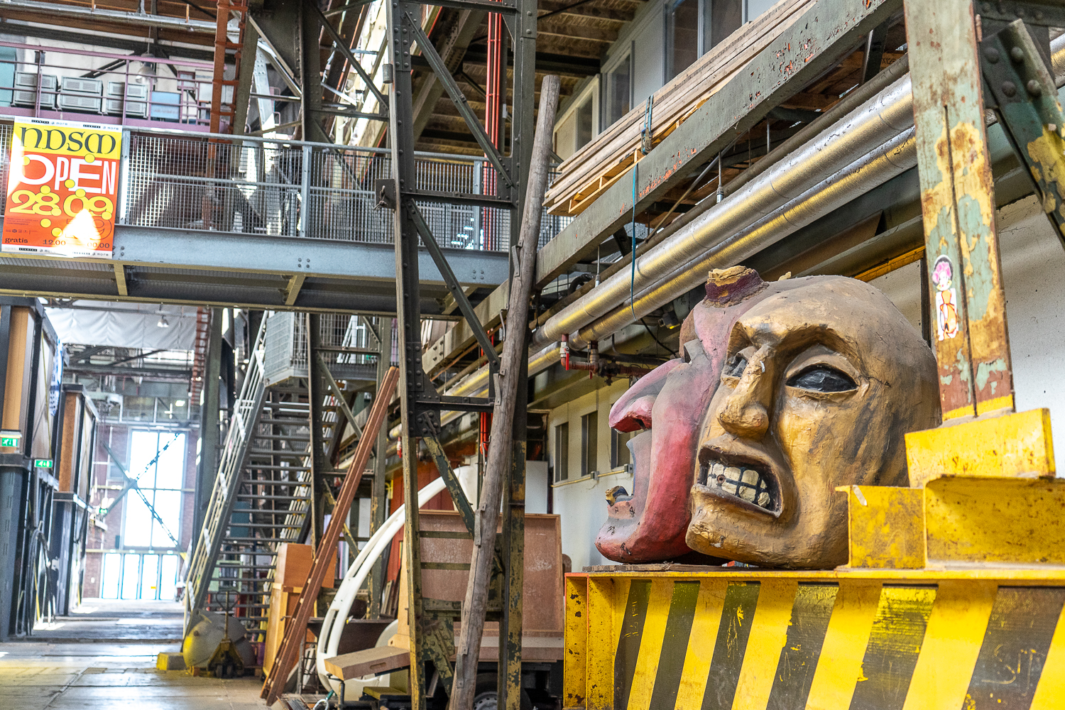 An industrial building with large sculptures of theatre masks in the foreground