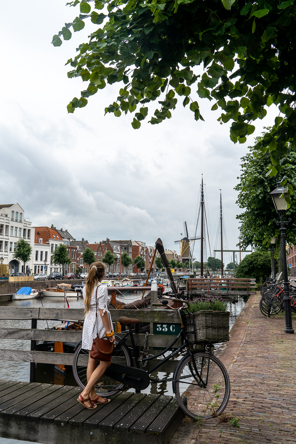 A girl standing in the old canals in Rotterdam next to a classic looking bicycle