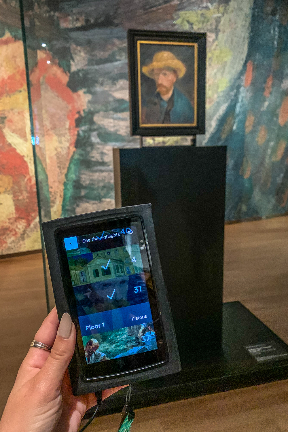 Holding an audio guide inside Van Gogh Museum with self portrait of Van Gogh in background