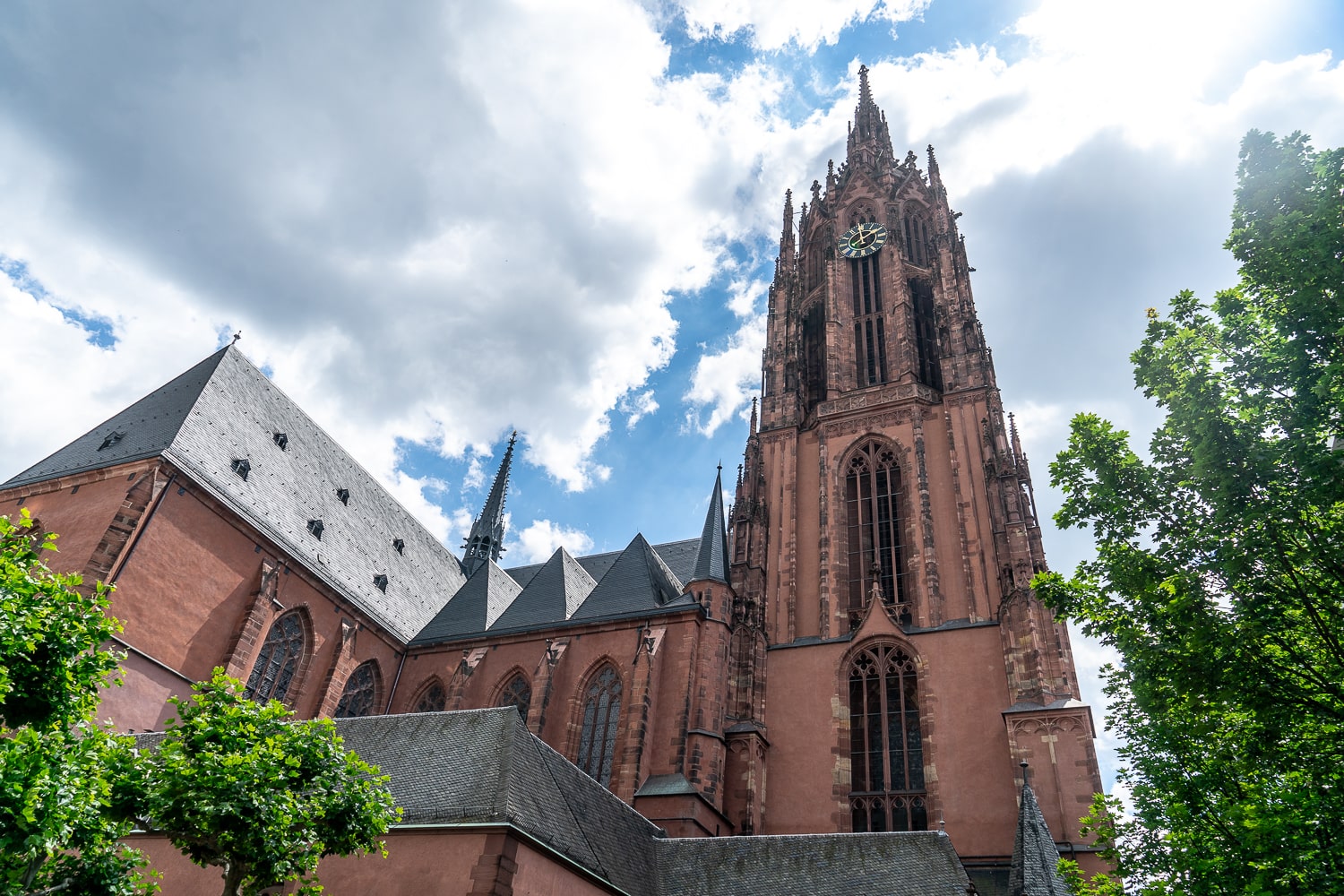 A red gothic church on a sunny day framed by trees