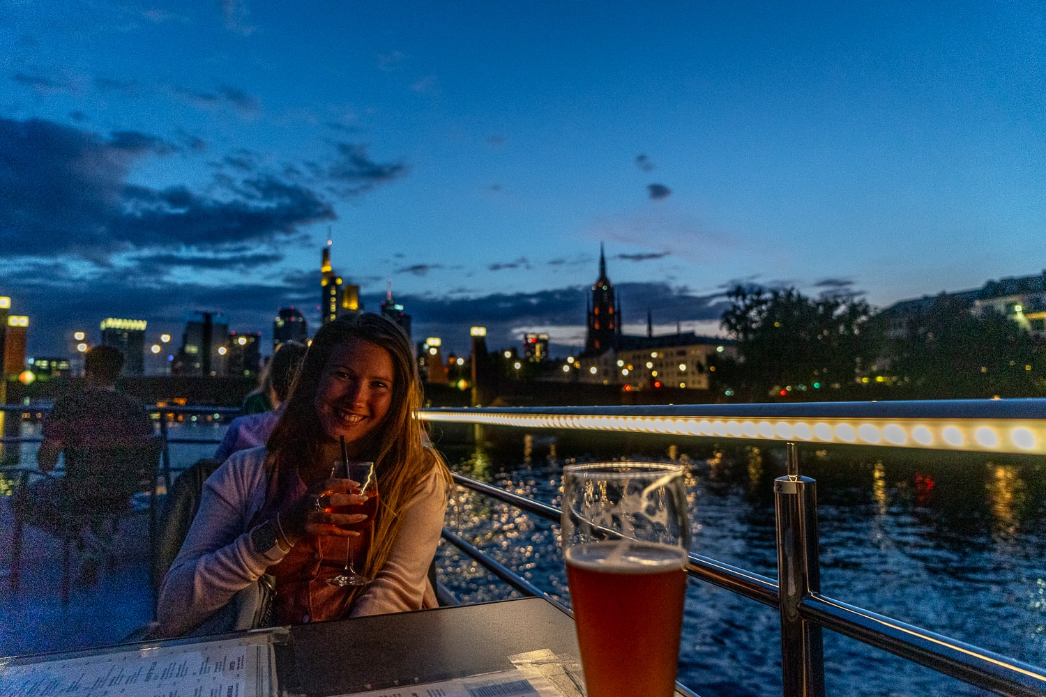 A girl sat on a night river cruise boat with beers
