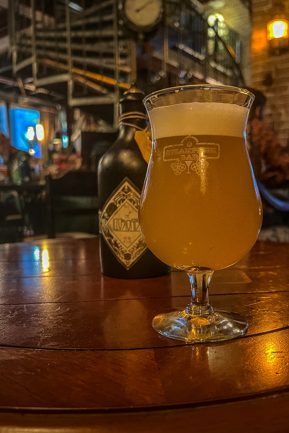 A craft beer on a dark wood table inside a low lit bar