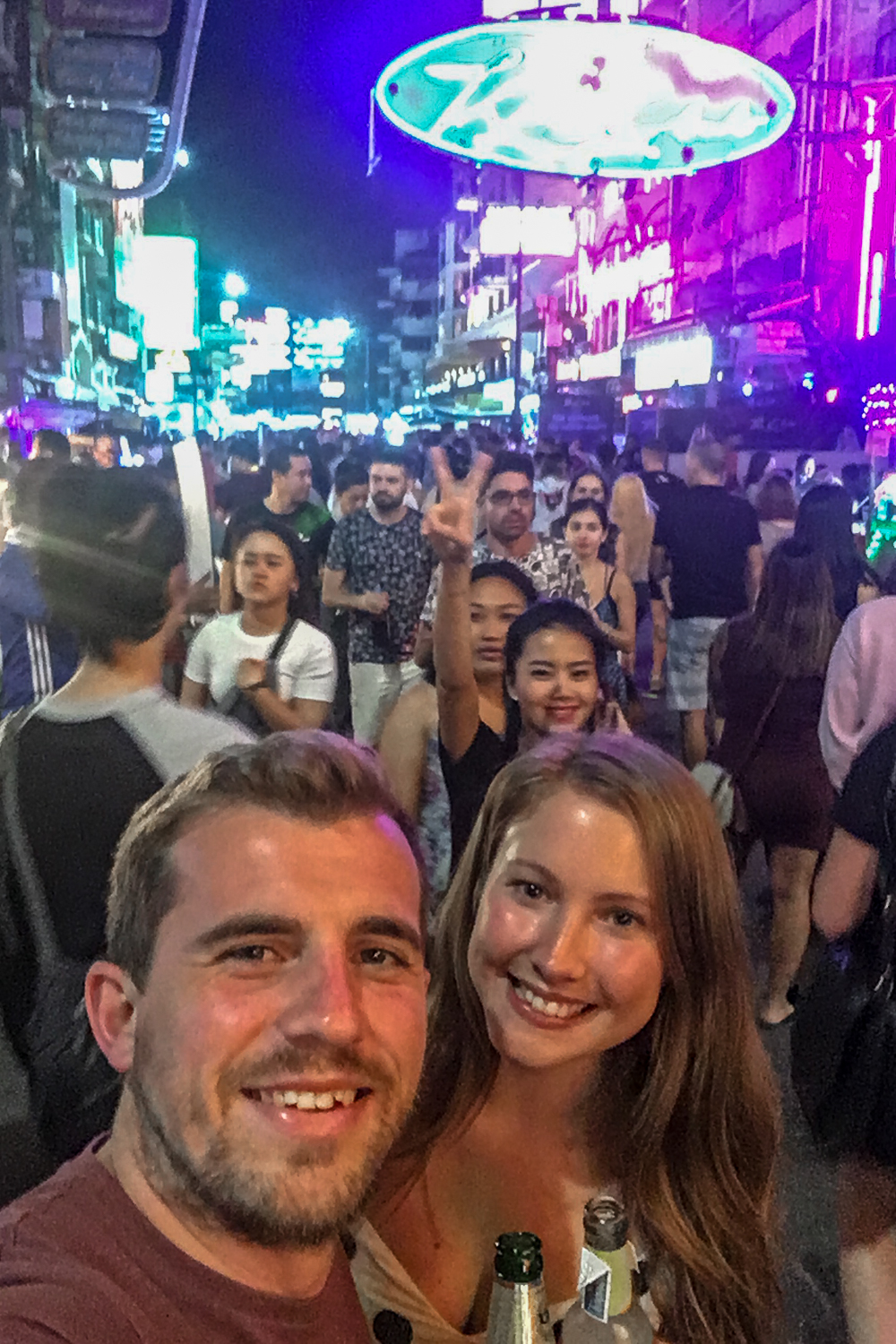 A selfie of a couple on a busy Bangkok road with hundreds of people and neon lights