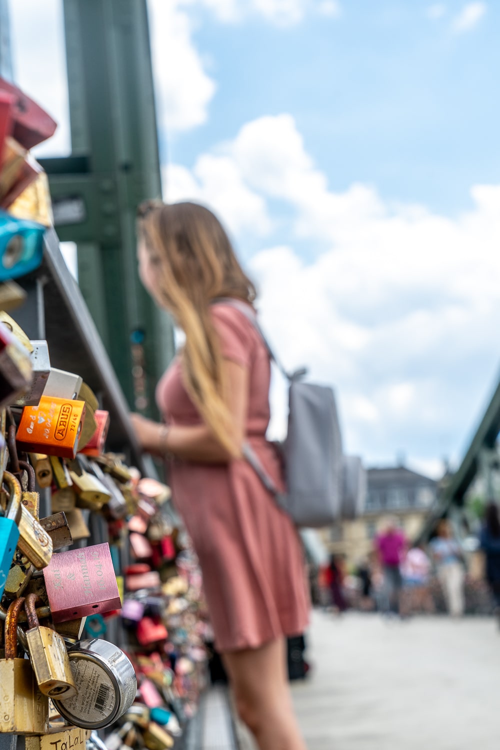 A close-up of love lock padlocks on an iron bridge with a girl in the background