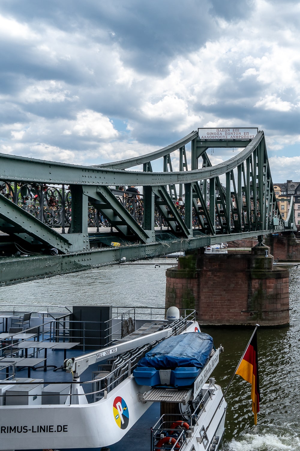 A sage coloured, industrial looking bridge over the river with a river cruise boat beneath