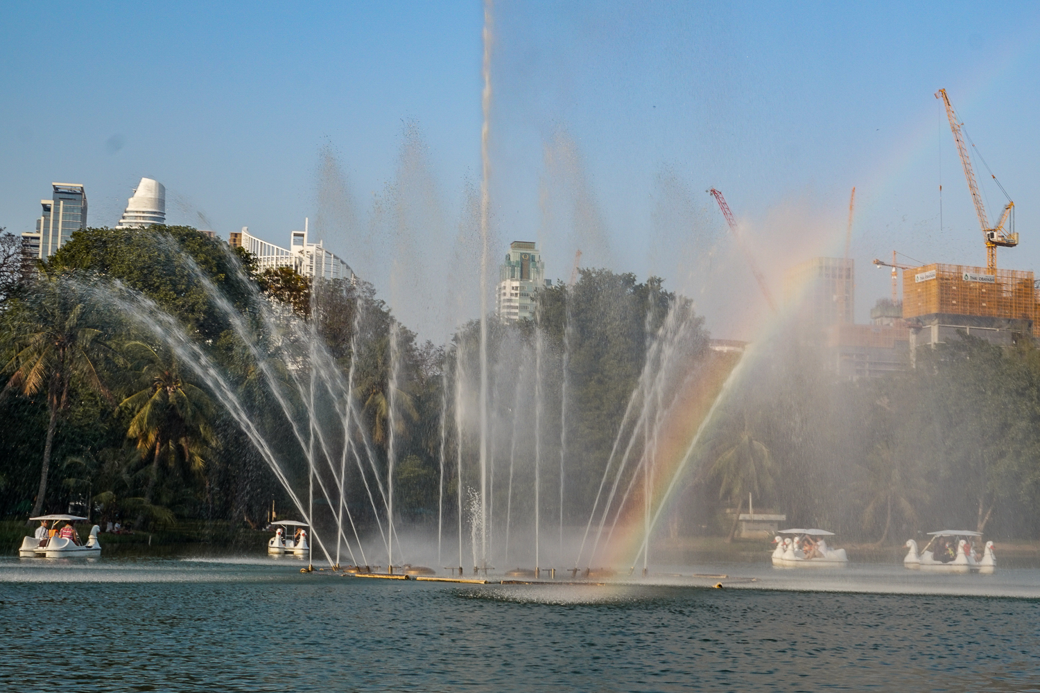 Large fountains creating a rainbow on a lake with boats