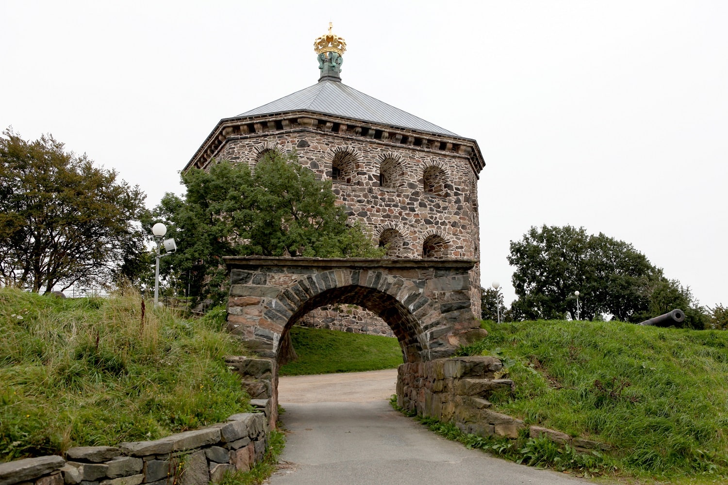 A stone fort on top of a hill in Sweden with a stone bridge in front of it