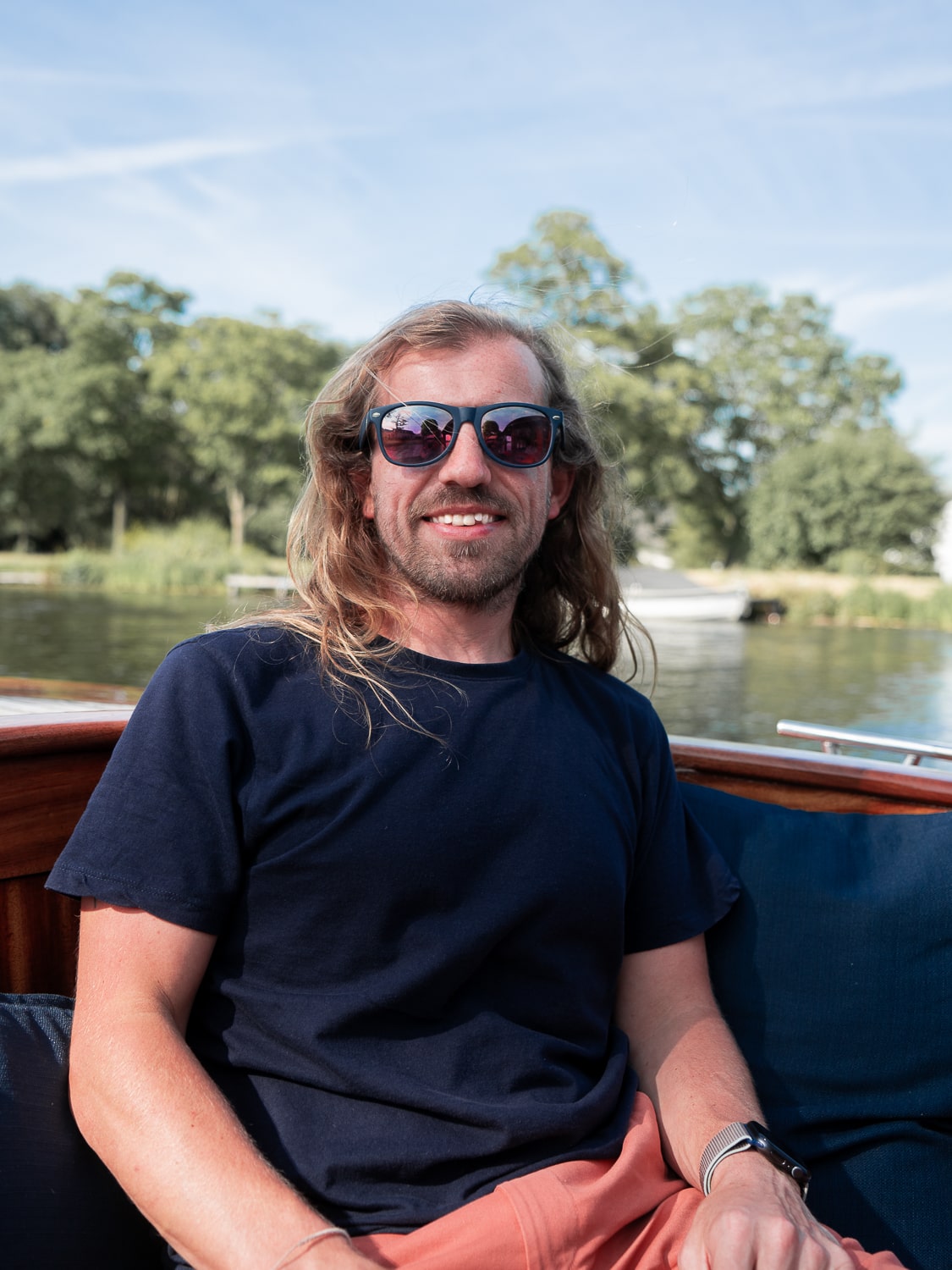 A man sat on a wooden saloon boat on a lake with trees in the background
