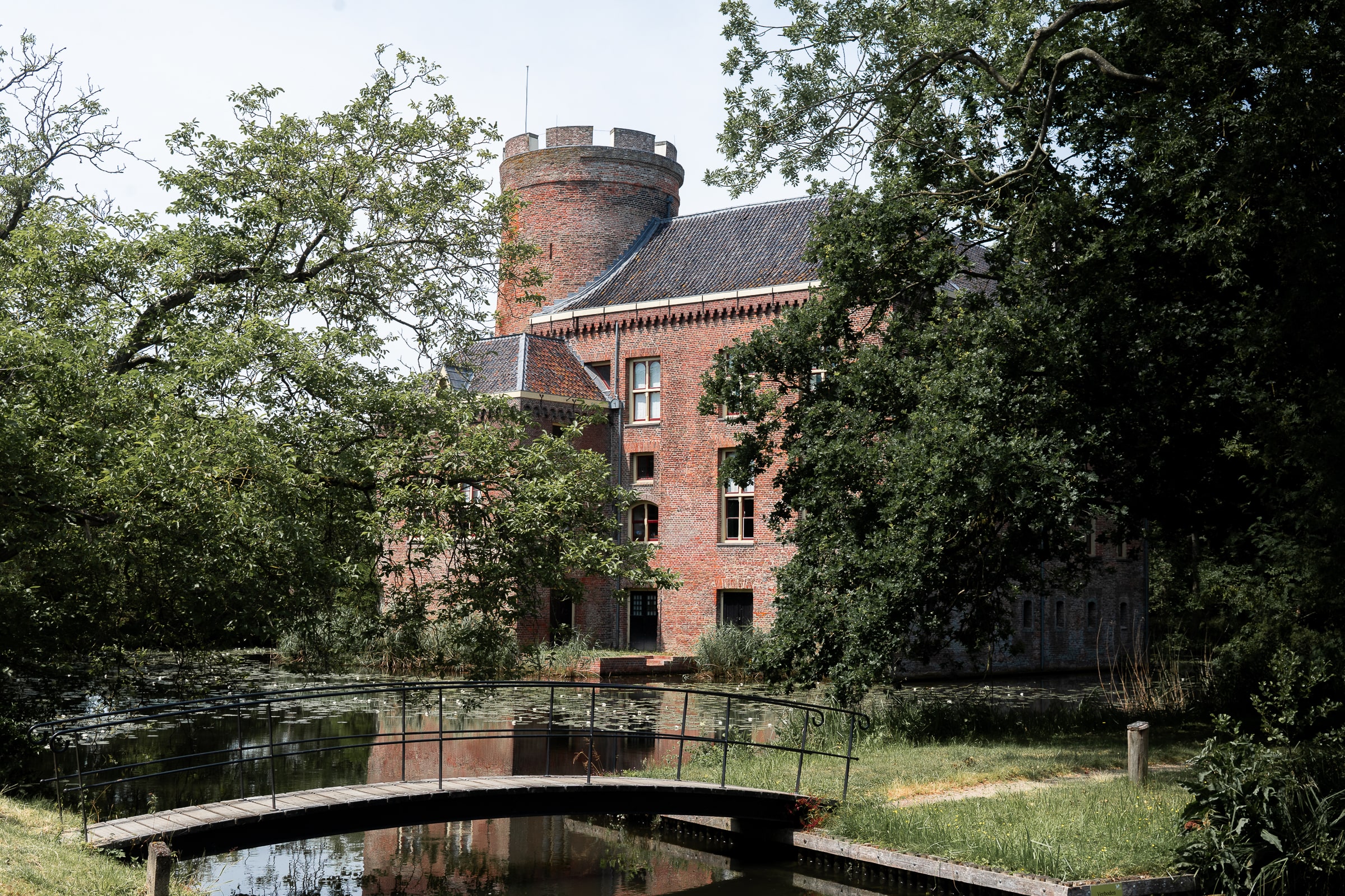 A red brick castle with a small bridge crossing the moat amongst trees