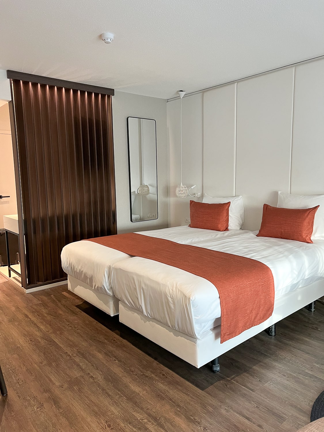 A hotel room with white bedding and peachy-orange throws and cushions