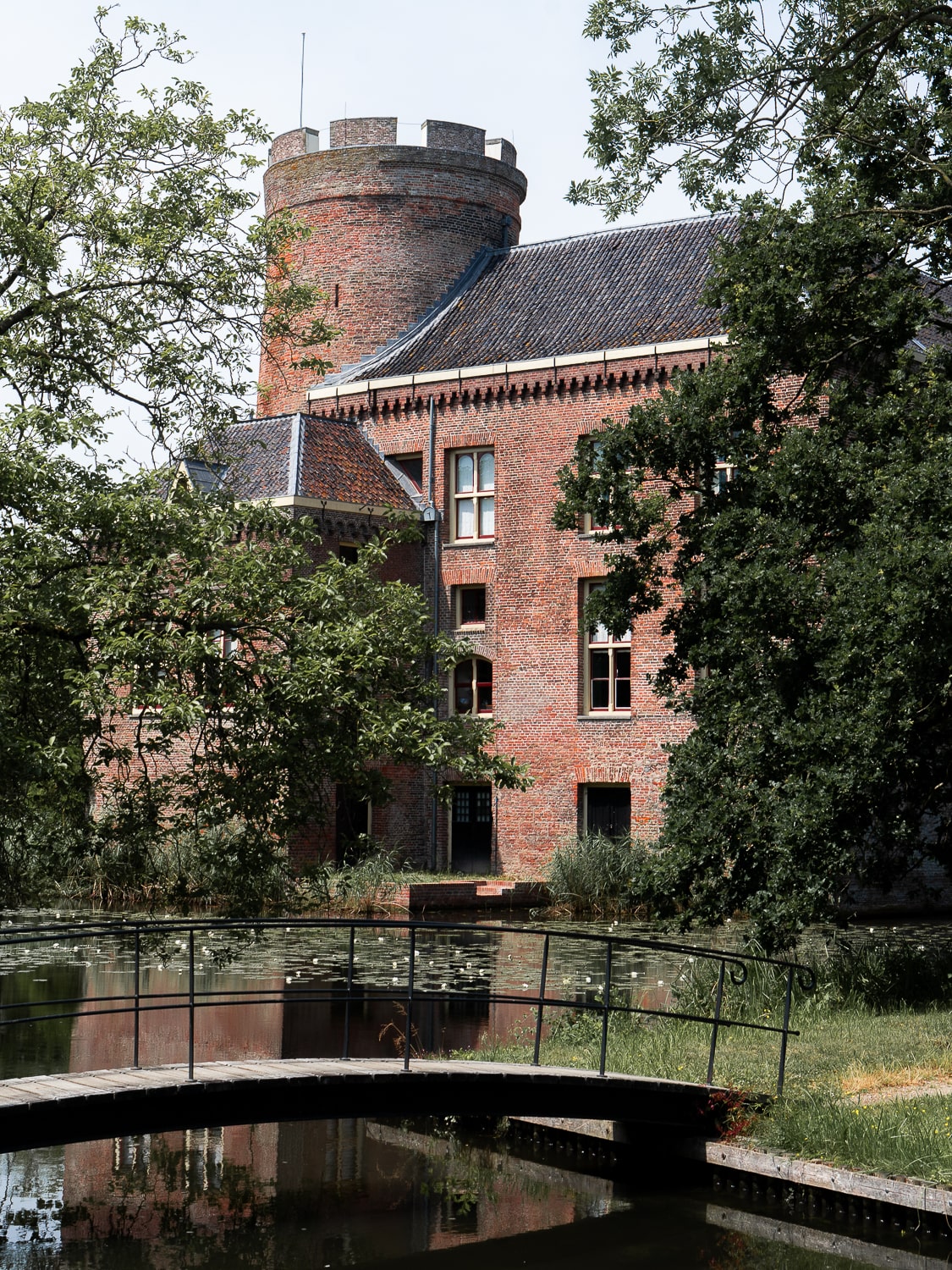 A red brick castle with a small bridge crossing the water amongst trees
