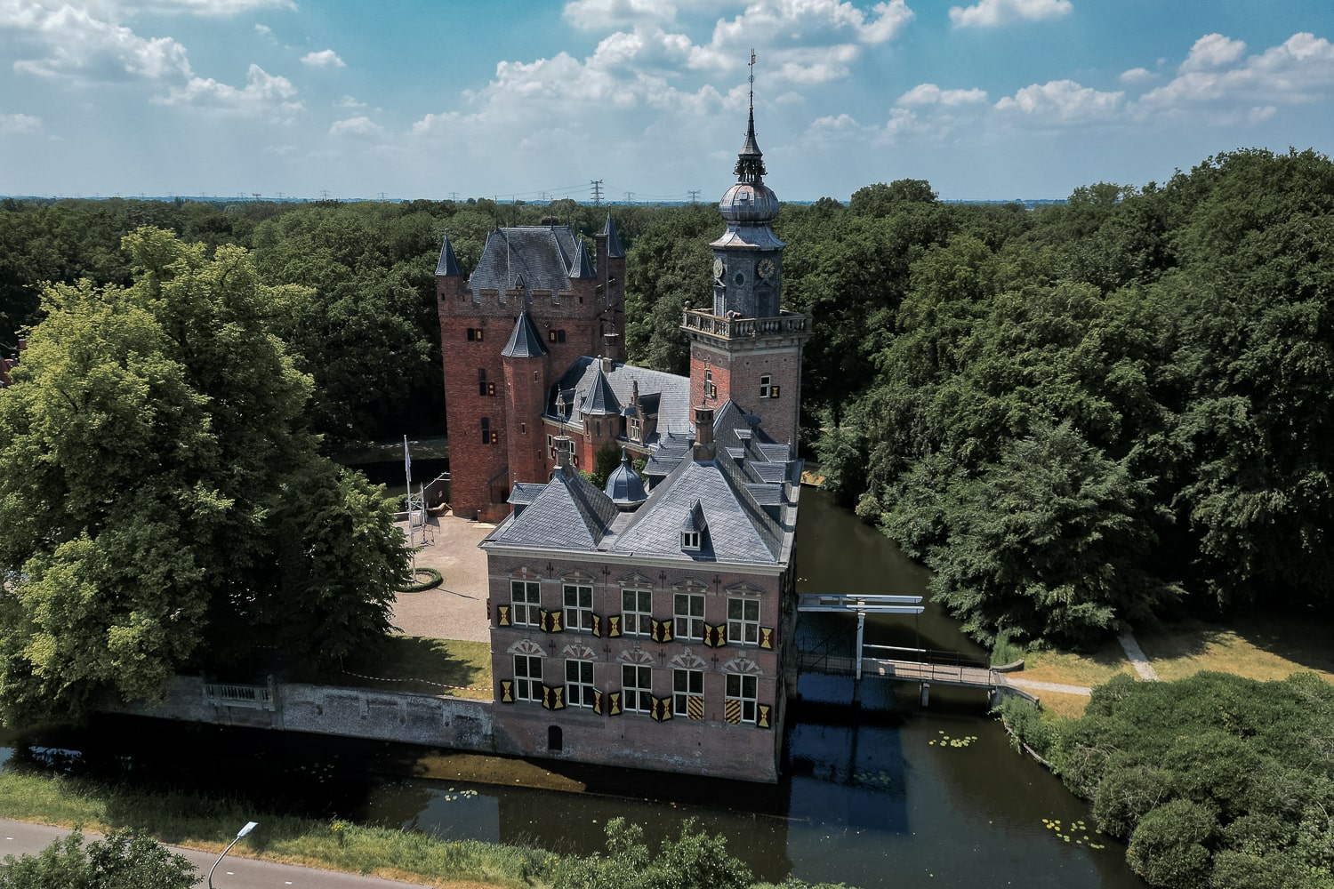 An aerial shot of a red brick Dutch castle surrounded by water and a forest