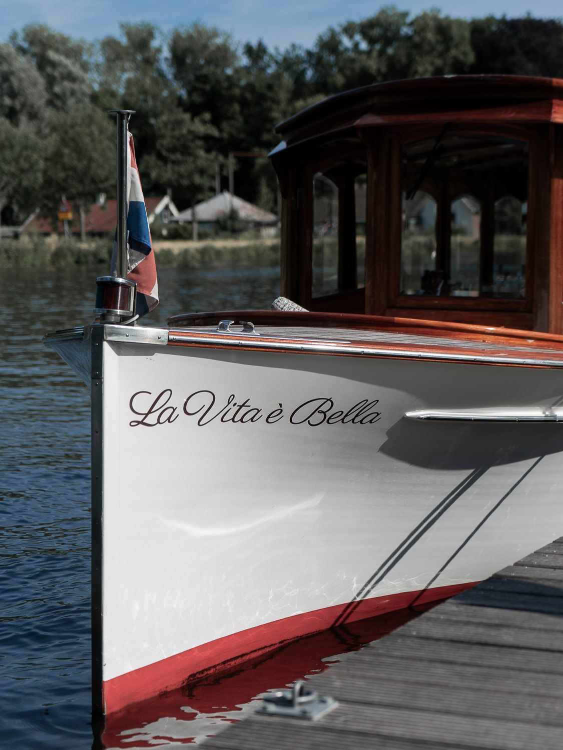 A white saloon boat with dark wooden sides and roof with the name "La Vita e Bella" painted in fancy font