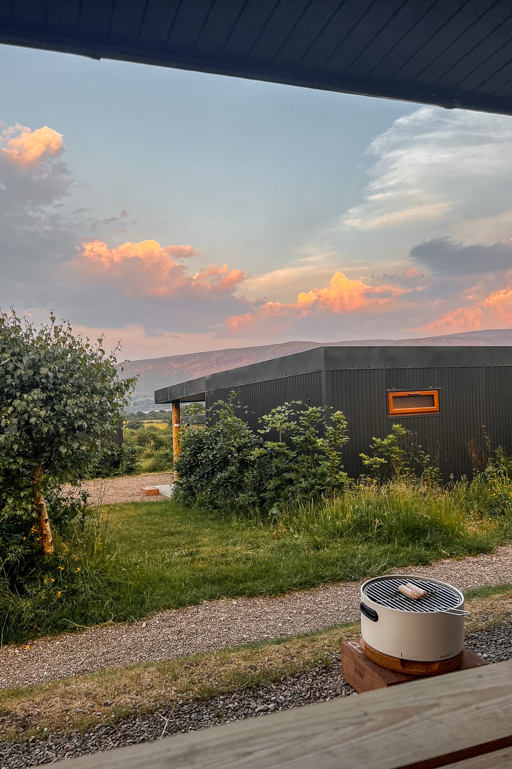 a barbecue on a patio on a glamping site with a pink sunset