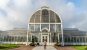 A girl walking towards a large palmhouse made of glass and white steel, a typical 19th century style