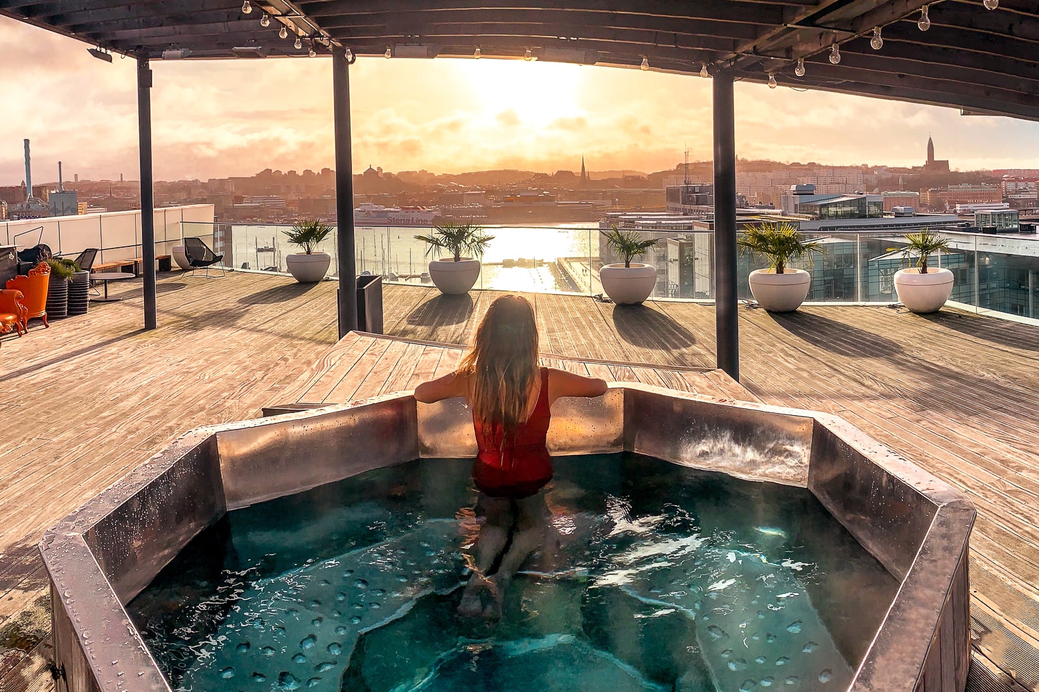 A girl in a jacuzzi on the rooftop of a hotel looking out at the sun rising over Gothenburg