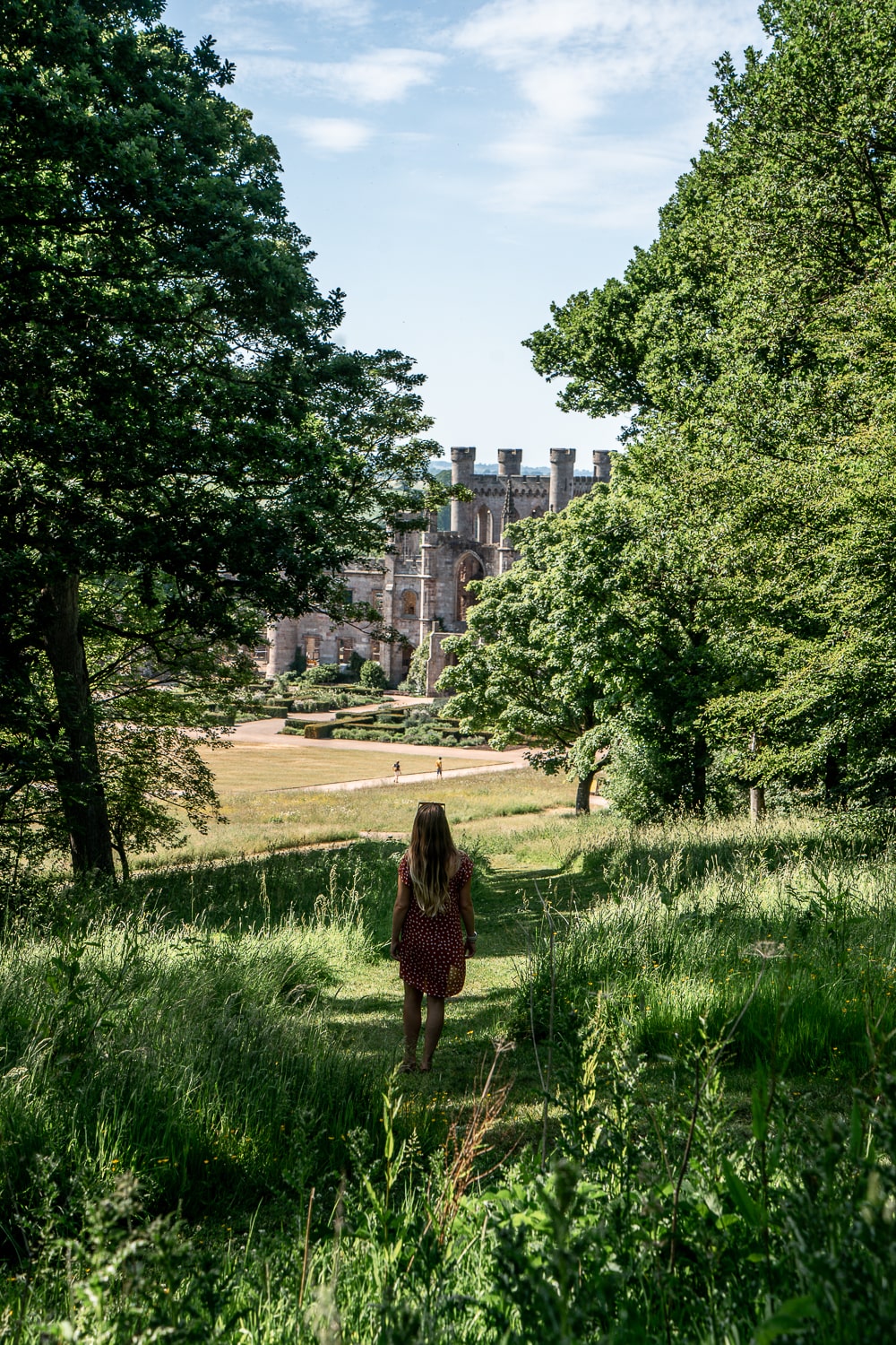 a girl walking on the lawn towards a large gothic castle with battlements