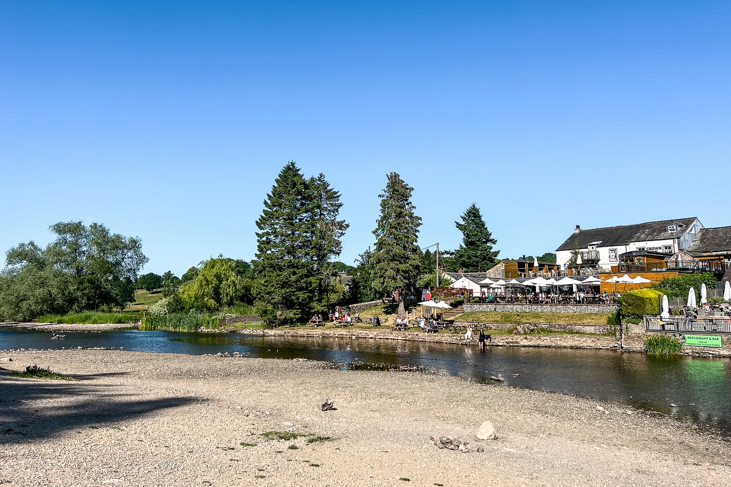 a river running next to a pub with a busy beer garden