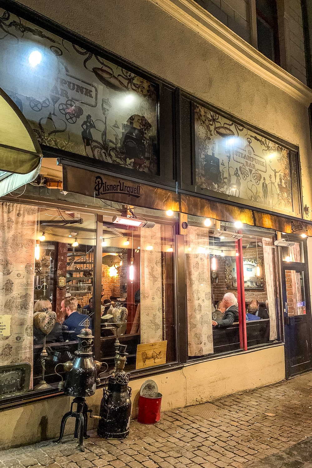 Outside of a craft beer bar at night with warm orange, glowing lights and a steampunk look