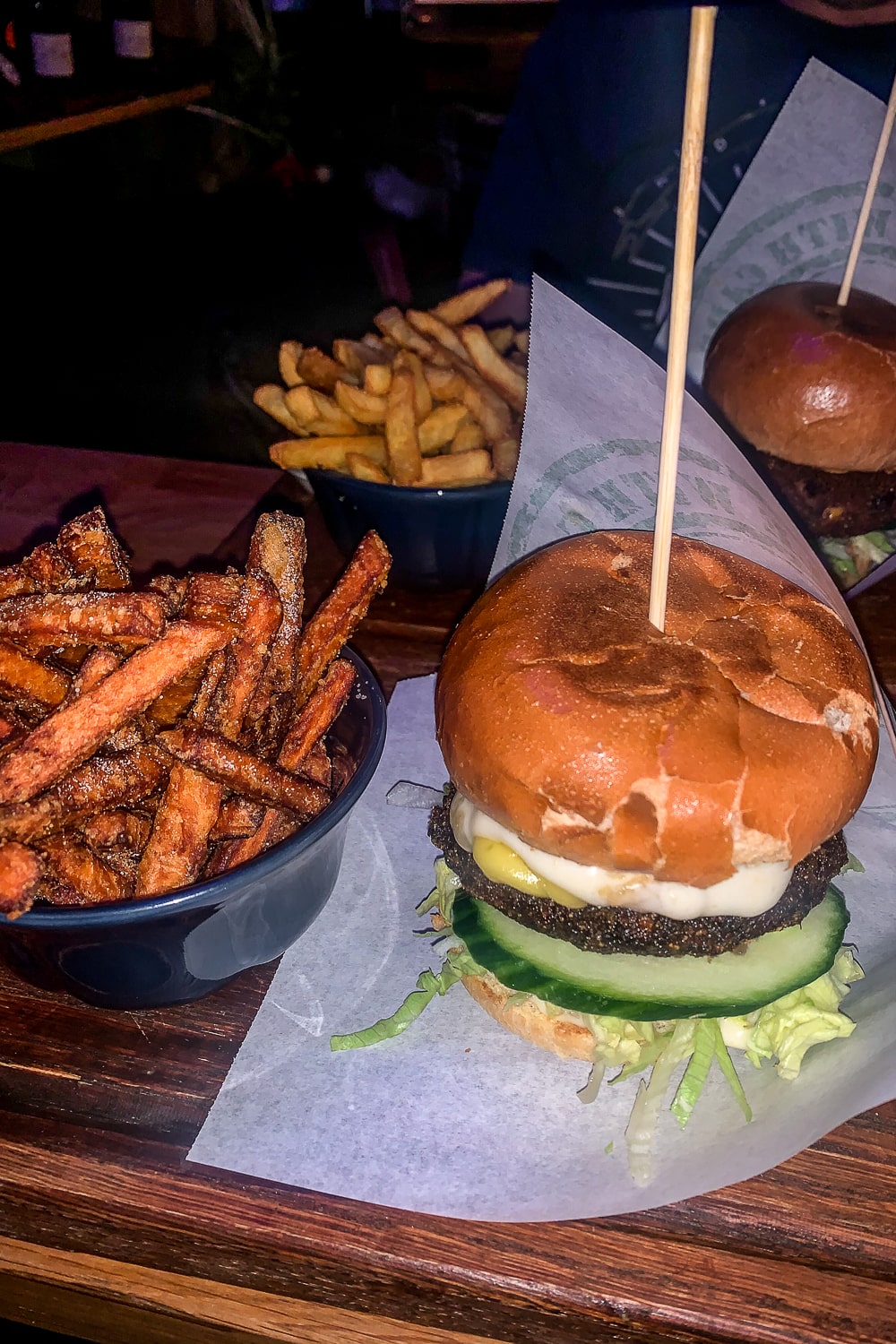 Two tall stacked vegan burgers with bowls of seasoned fries