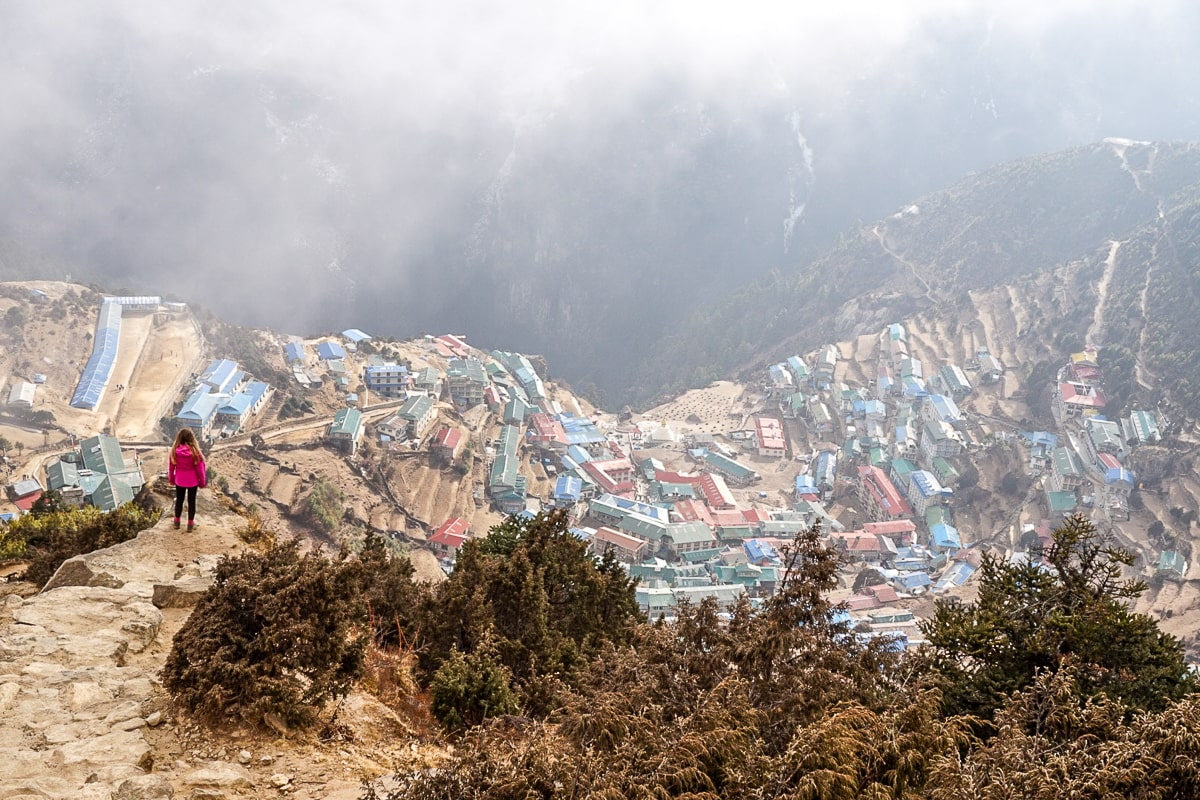 A woman stadning overlooking the Himalayan village of Namche Bazaar - a crowded collection of small dwellings with colorful metal rooves