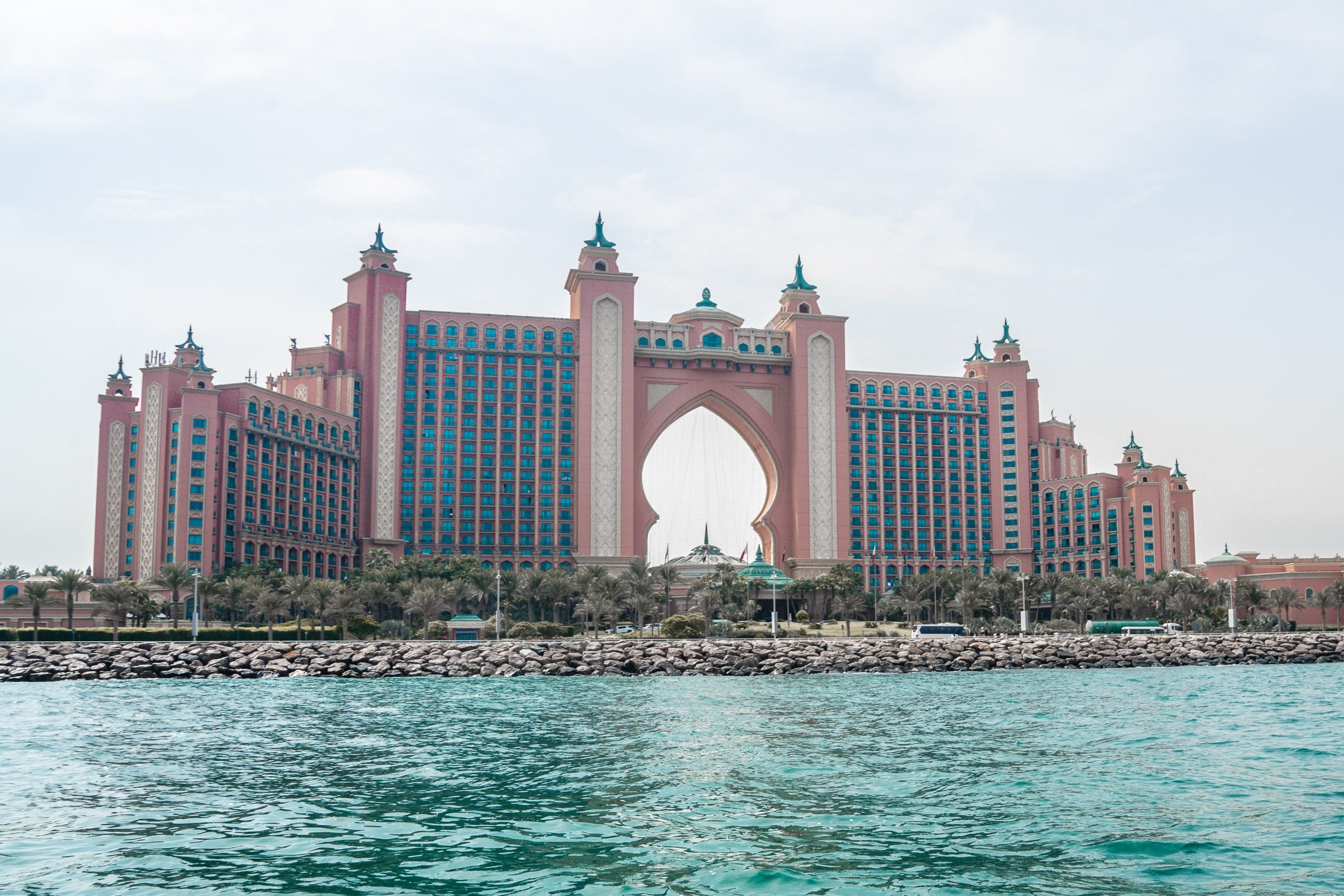 The Atlantis Hotel in Dubai from the water. A grand hotel with pink coloured stone and a large keyhole shape in the center of the building