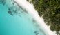 A top down view of a Maldives beach with a vibrant blue sea and a dark green treeline on either side