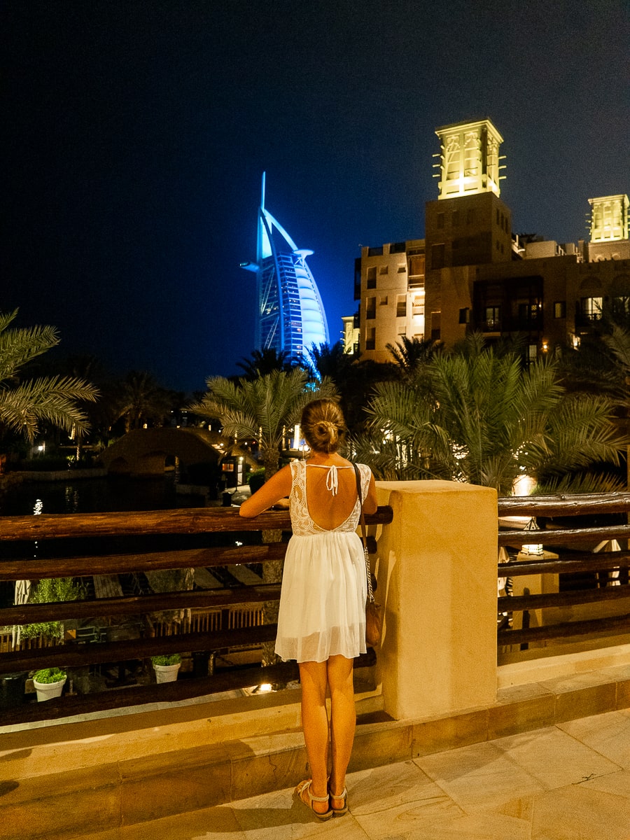 A girl looking from a balcony at the Burj al Arab lit p in a blueish color at night