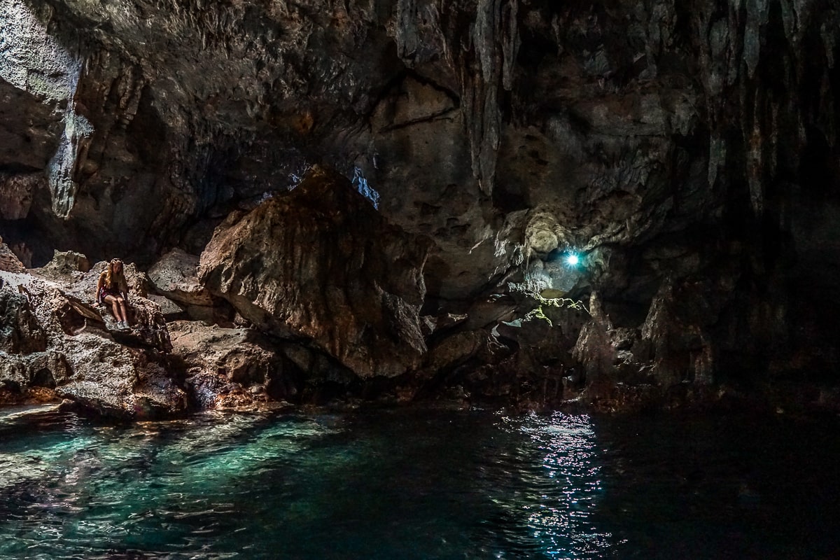 A dark interior of a limestone cave with a clear blue pool