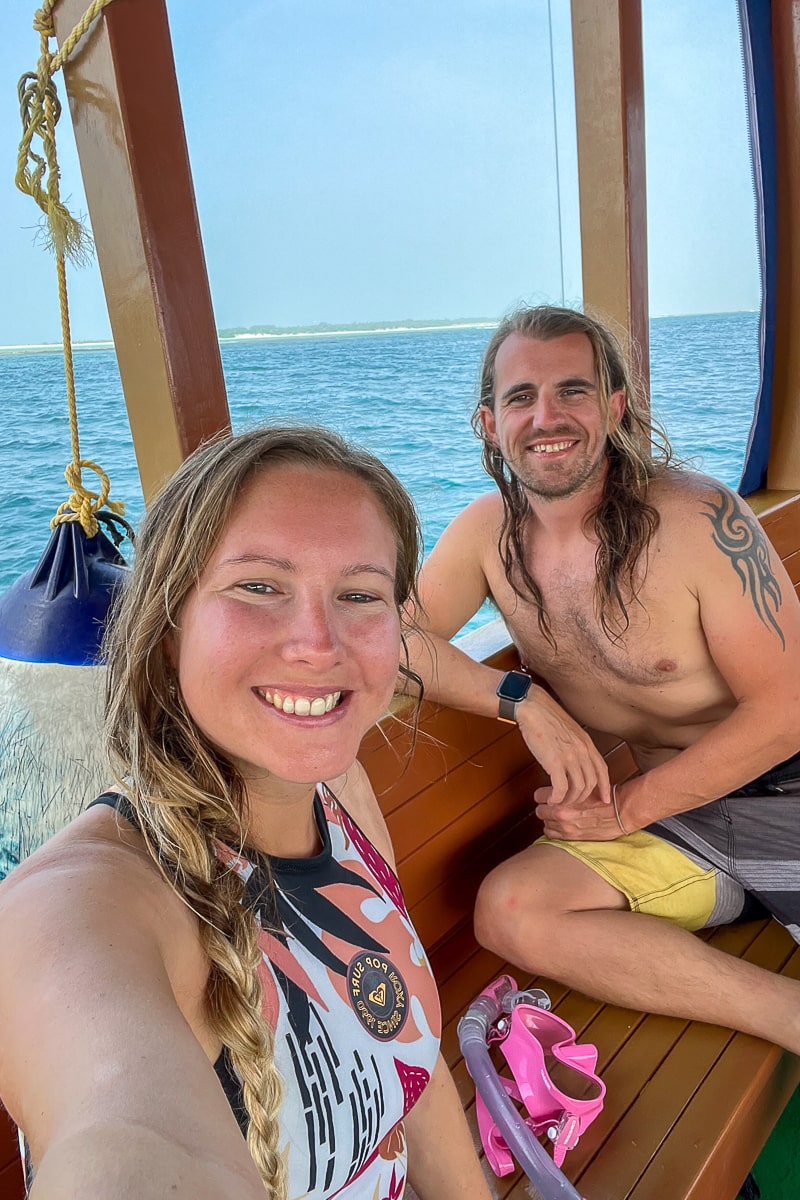 A couple sat smiling on a boat in swimwear