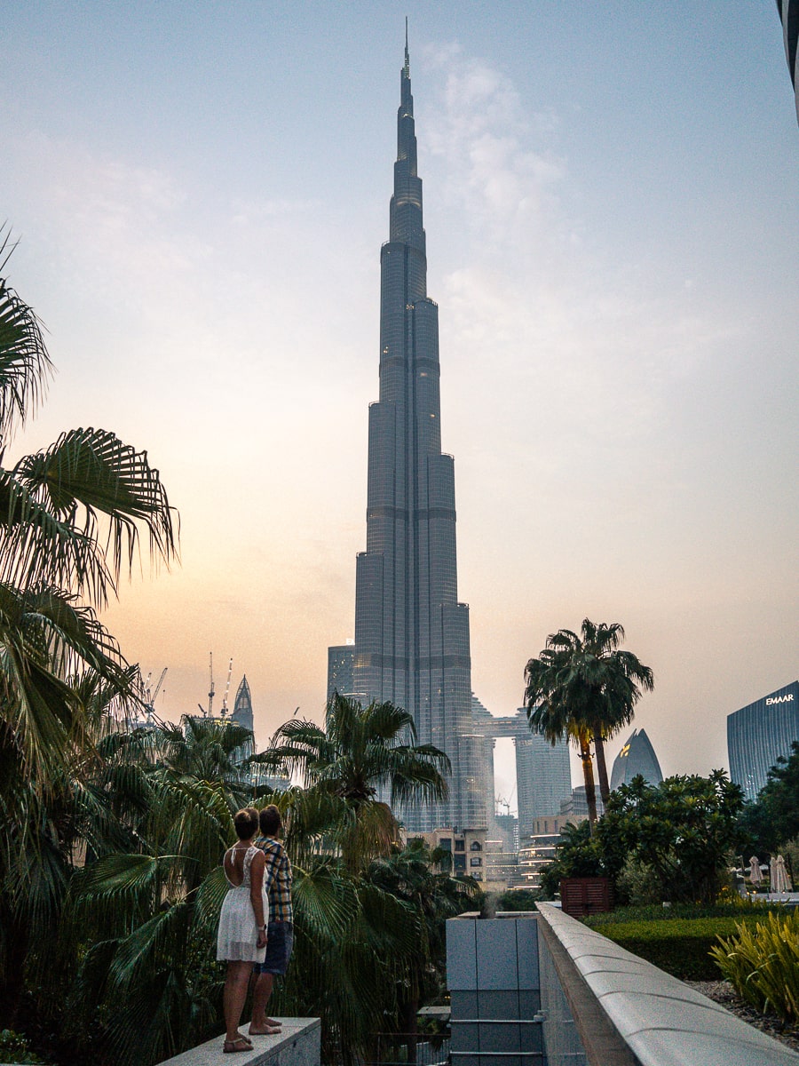 The Burj Khalifa towering over some palms and a couple looking up at it