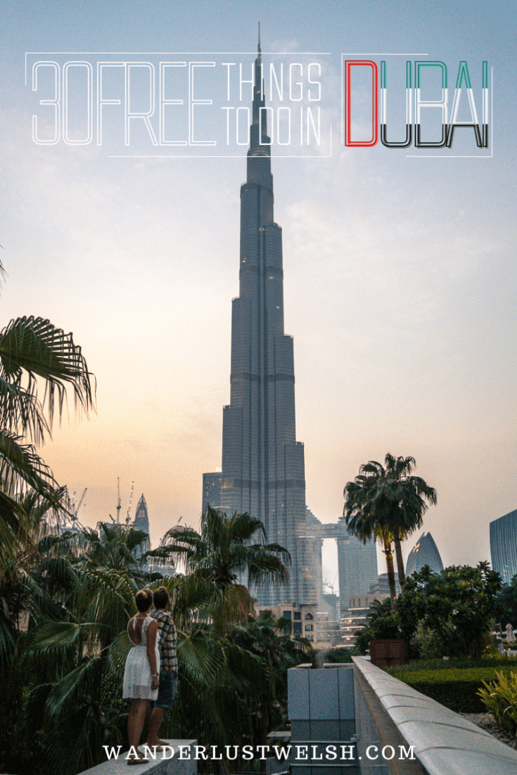 A couple on a wall near palm trees looking up at the Burj Khalifa towering over