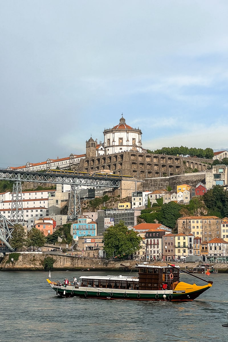 A river boat passing by and a bridge and hillside with buildings behind