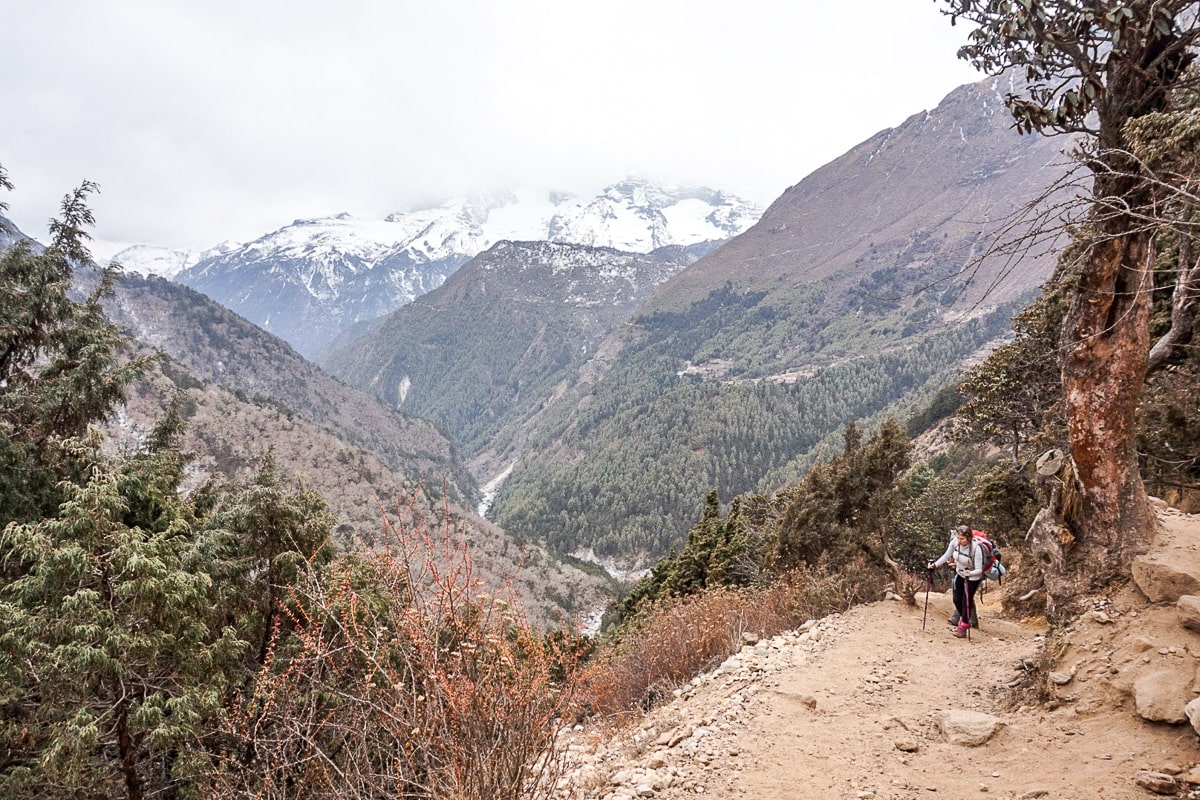 A woman hiking along a dusty trail with a view of a deep river gorge and mountains covered in evergreen trees