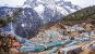 A wide view of Namche Bazaar from above. Metal coloured roofs, evergreen trees, and huge snowy mountains