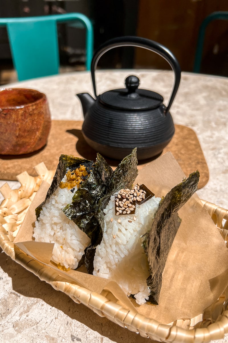 Two rolls of nori with sushi rice and a small cast iron teapot behind
