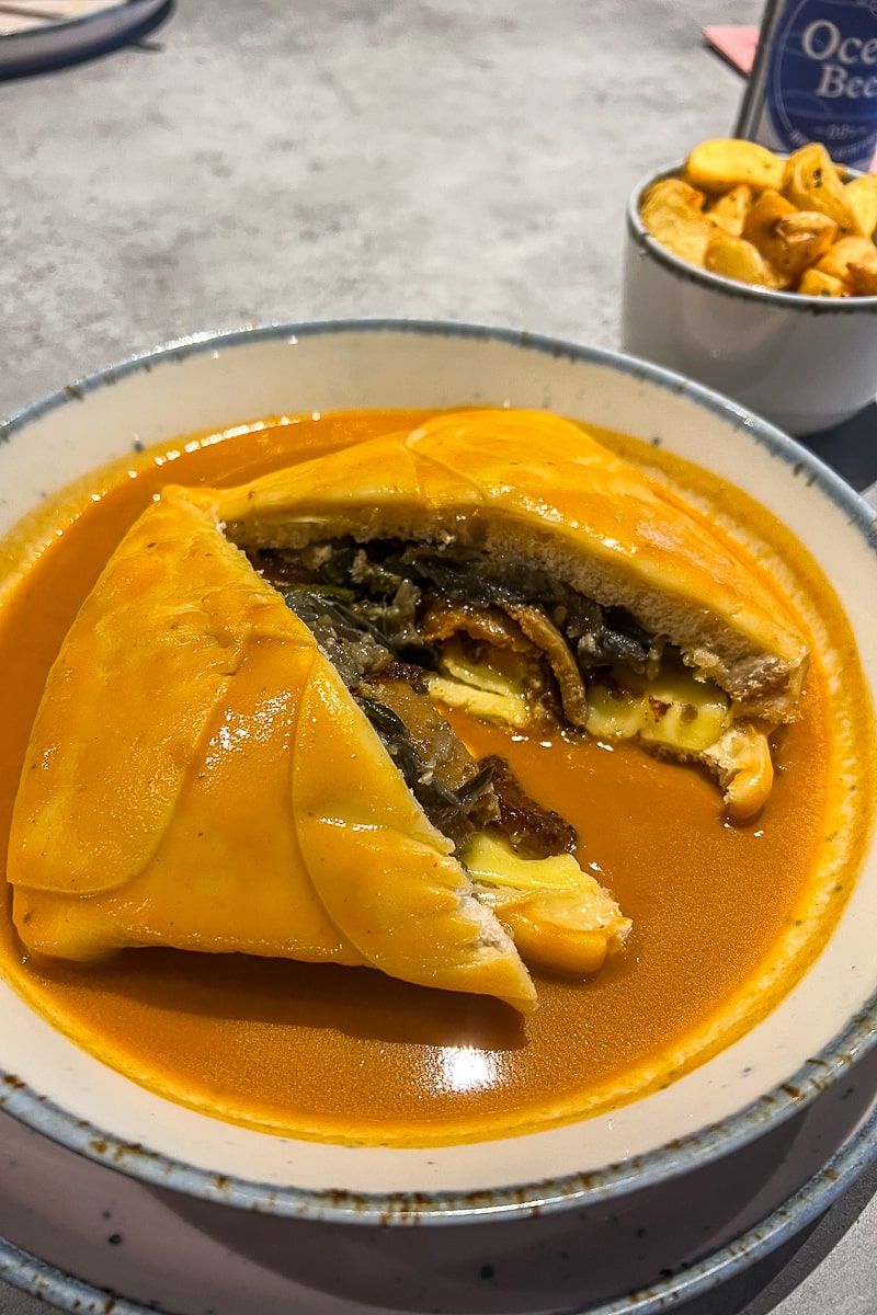 A sandwich covered in gravy cut open with vegan meat and vegetables spilling out