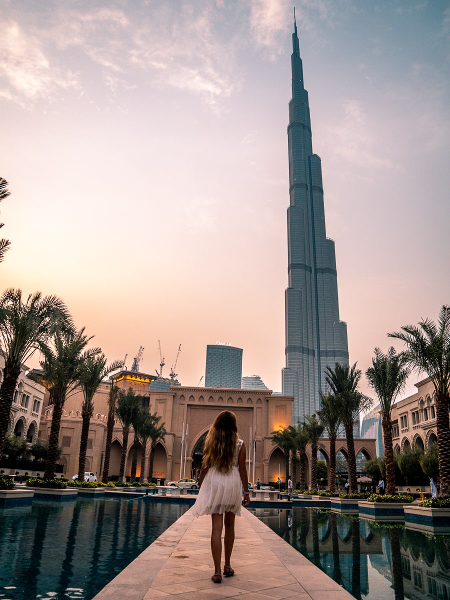 A girl walking along a stone walkway between two water features with the Burj Khalifa towering over