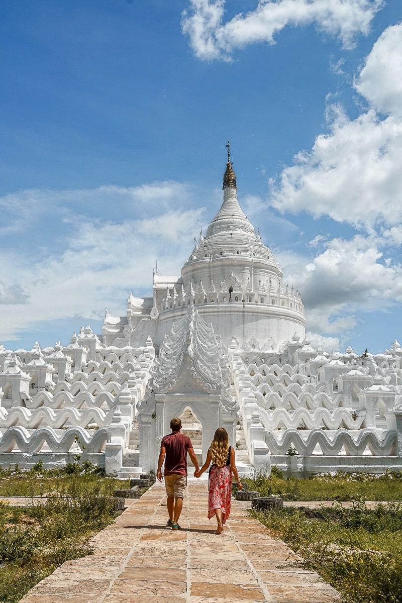 A couple walking hand-in-hand towards an intricate, white, wavy buddhist pagoda