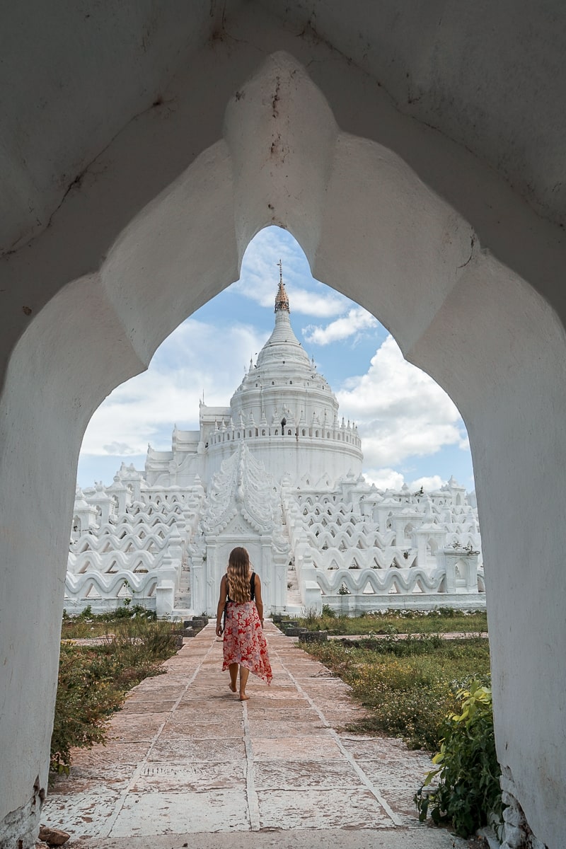 A woman walking towards a white wavy buddhist pagoda framed by a doorway