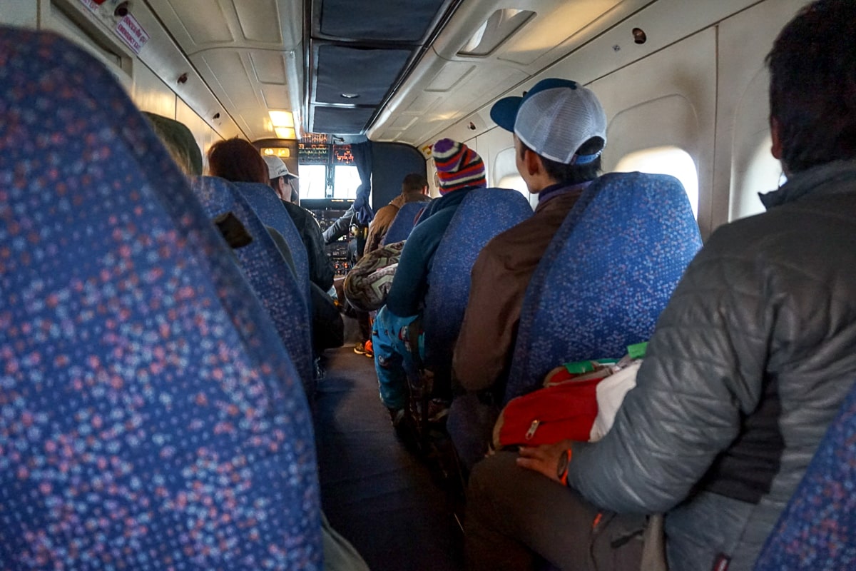 Inside a small prop plane with old, blue fabric seats which is full of people