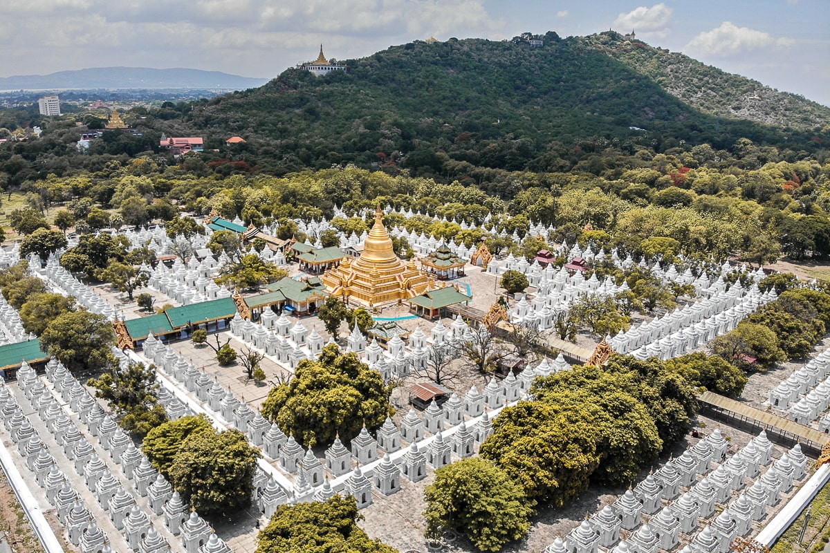 An aerial shot from a corner of a pagoda complex, hundreds of small white buildings surround the central golden stupa in square formations