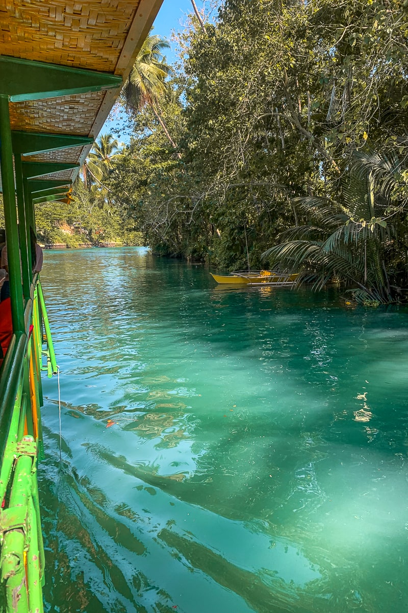 The clear blue Loboc river from a boat with a yellow kayak in the water