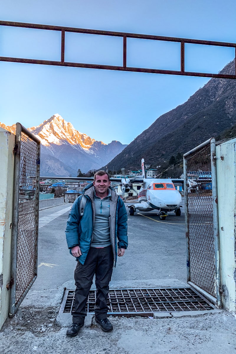 A man stood in trekking gear with a small plane behind him in Lukla airport