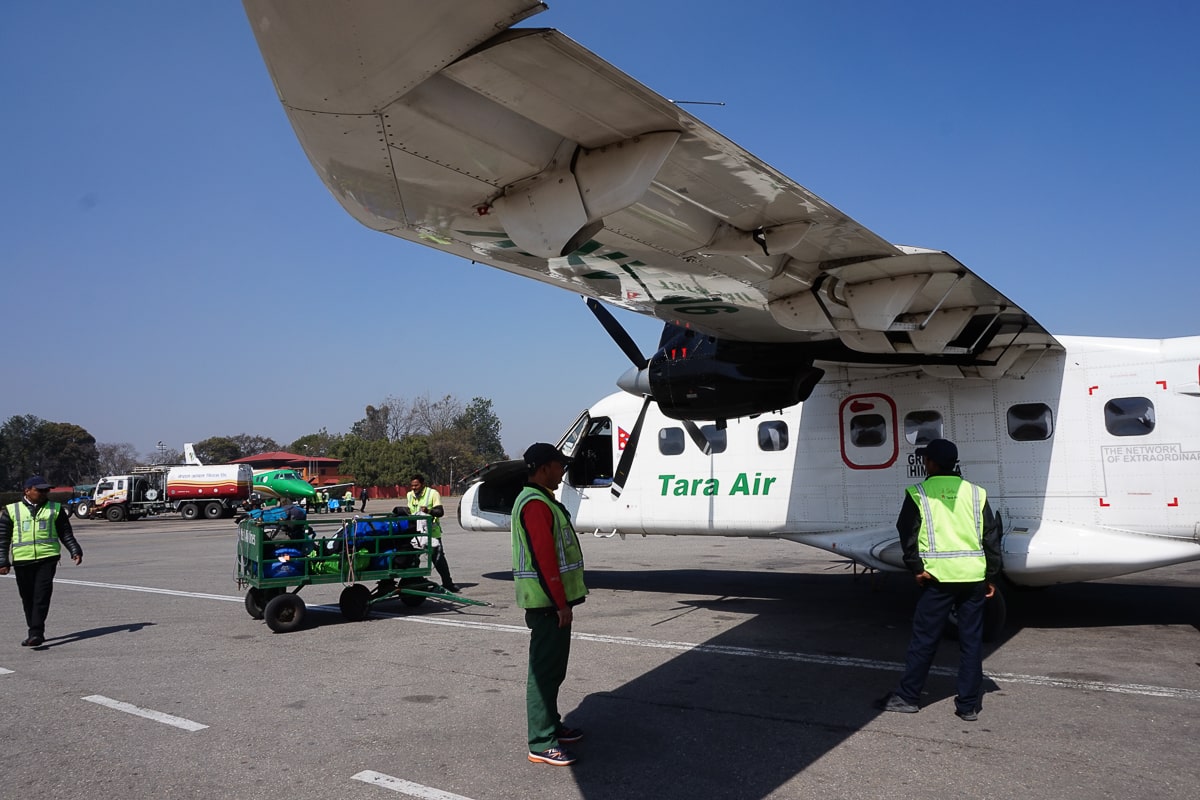 A small 'Tara Air' plane on the tiny Lukla runway. Baggage handlers are stood around in hi-vis jackets