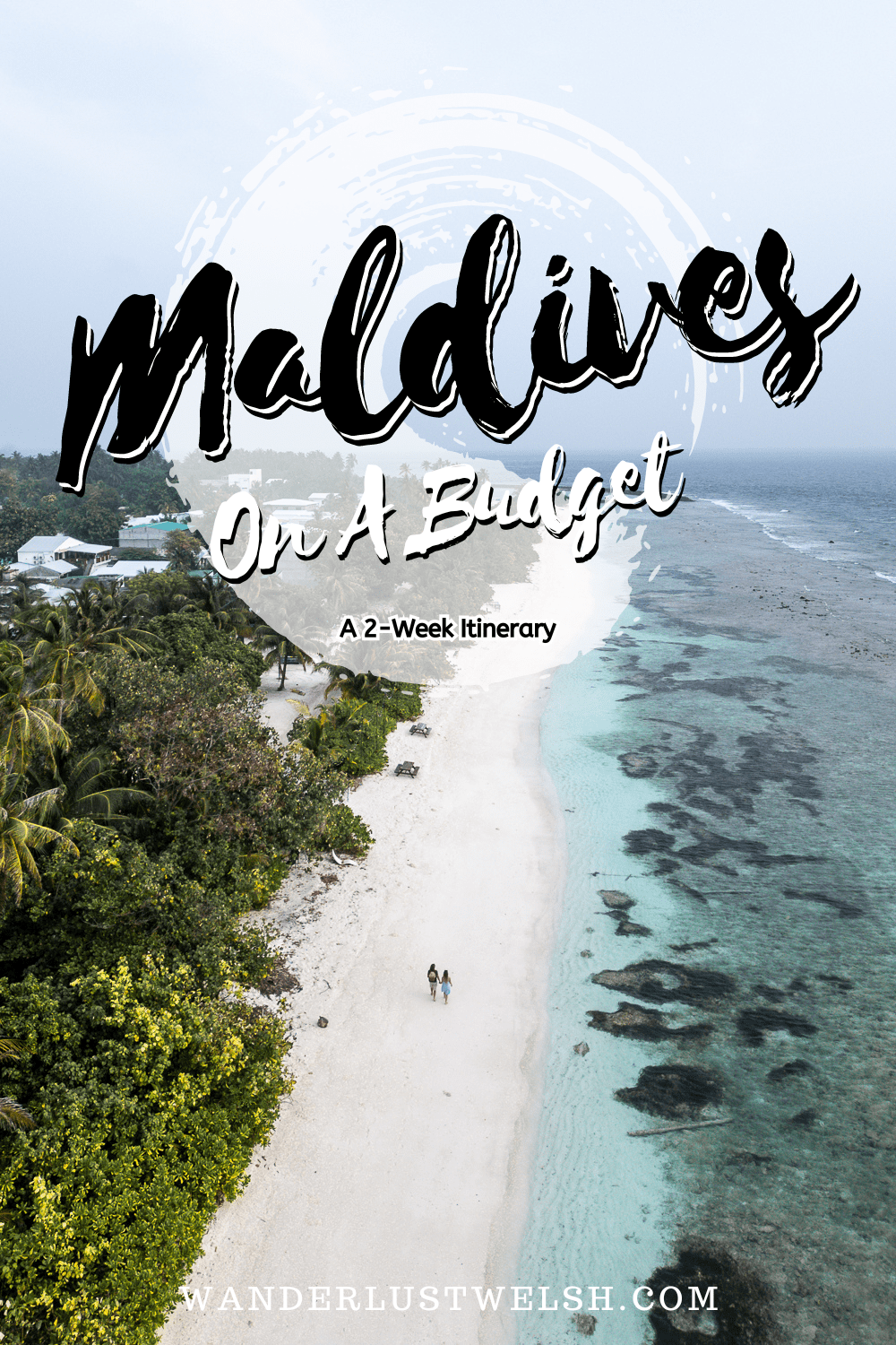 A couple walking along the beach in Dhigurah with a jungle to the left and ocean to the right