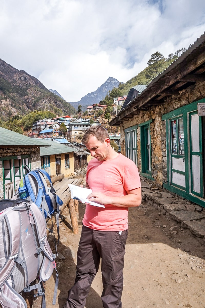 A man with rucksacks reading a guidebook in a Himalayan village