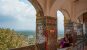 A woman sitting on a balcony decorated with gemstones and tiles looking out over a high viewpoint